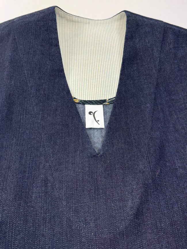 Robe ample sans manches en jean bleu marine, col en V, coupe trapèze fluide et contemporaine. Détail encolure